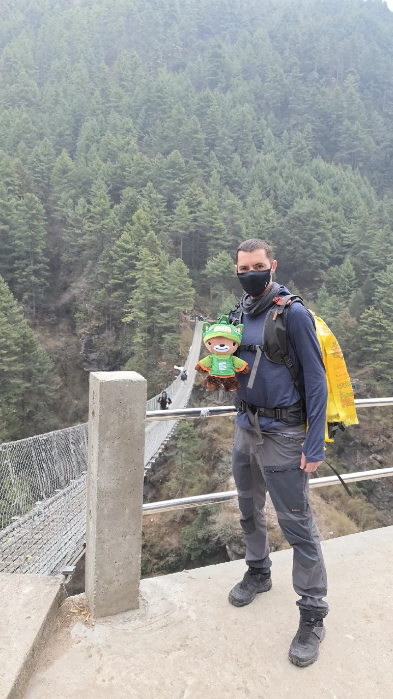 Nicholas holding Sumi at the entrance to the Hillary Bridge with a prayer flag draped like a cape