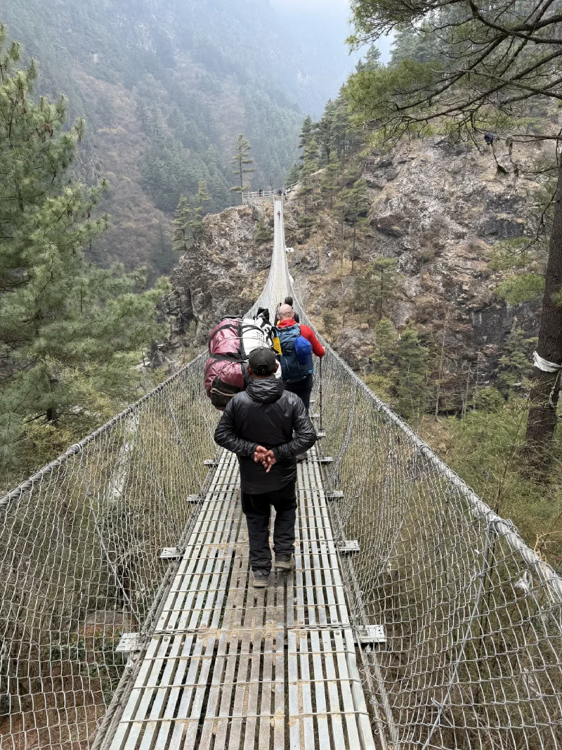 View from behind as the group crosses the Hillary Bridge with a porter carrying a massive load ahead