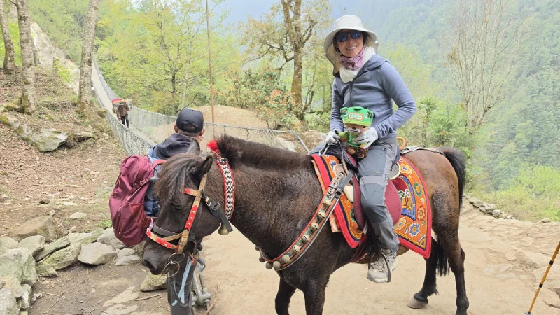 Pokin smiling on horseback holding Sumi, suspension bridge in the valley behind