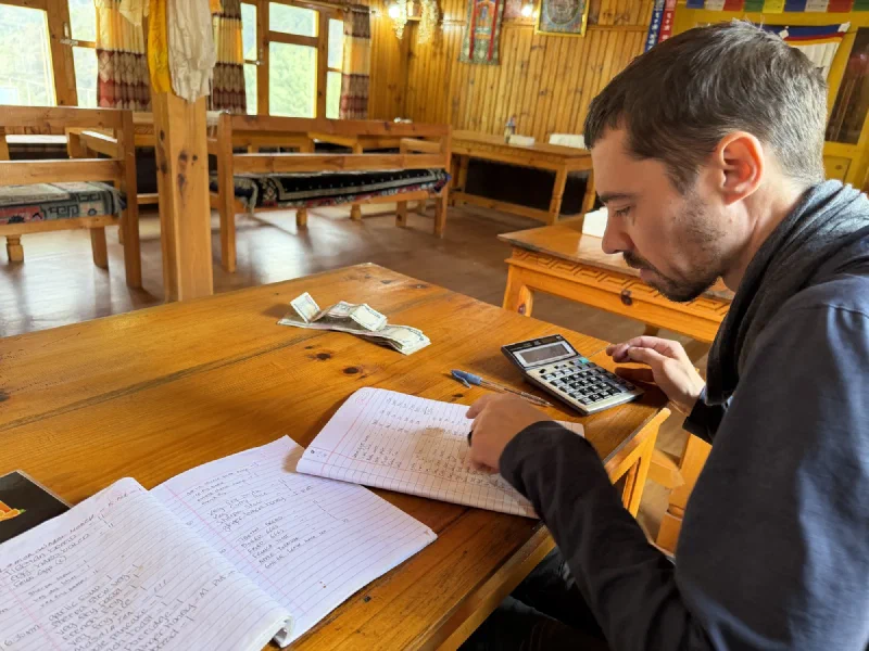 Nicholas at a wooden table using a calculator and notebooks to total up the food bill