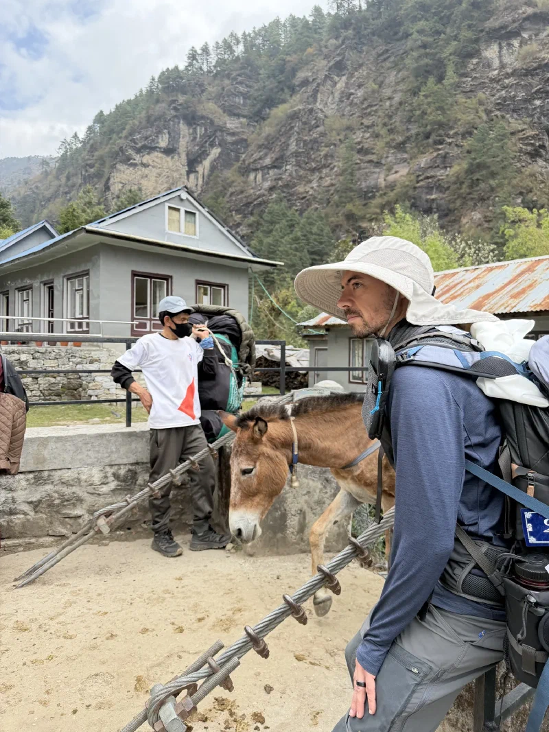 A trekker leaning on the bridge cable next to a local man and a waiting mule