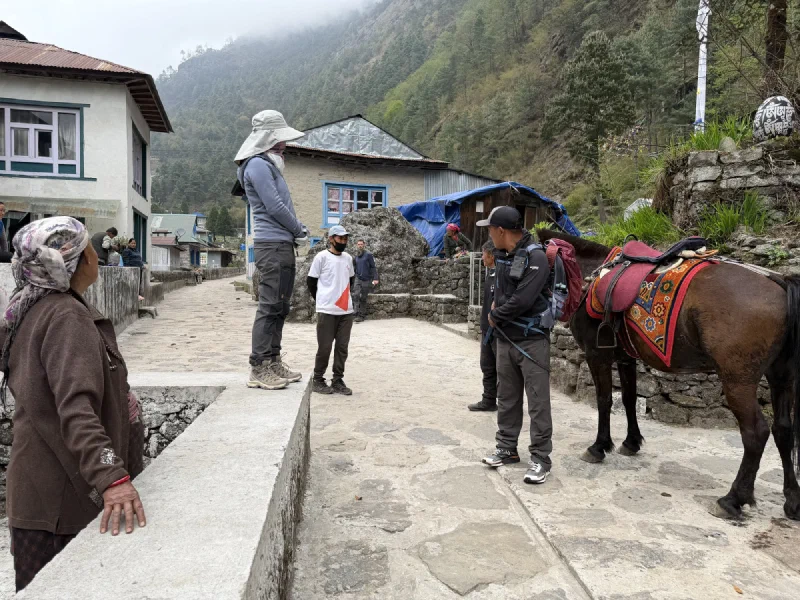 A saddled horse waiting on a village path while locals stand nearby