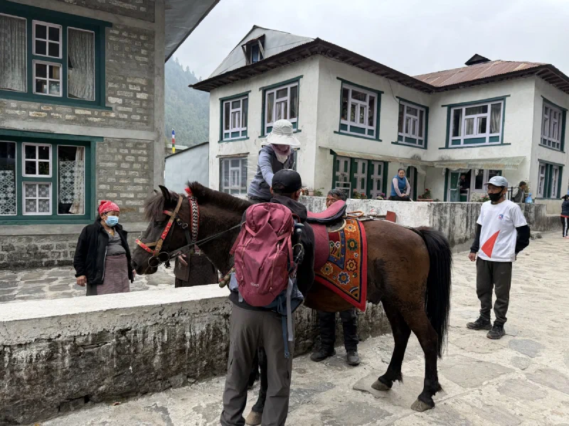 Pokin being helped up onto the dark brown horse in a village square