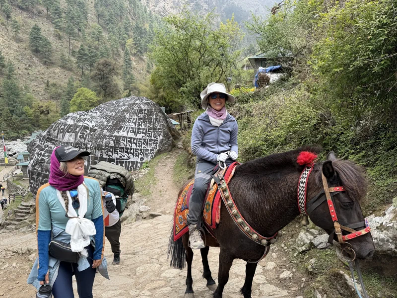 Pokin smiling on the horse beside a large boulder carved with Tibetan script