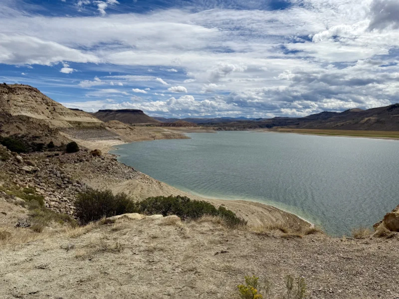 A wide turquoise reservoir between pale banded cliffs under a sky full of broken cloud
