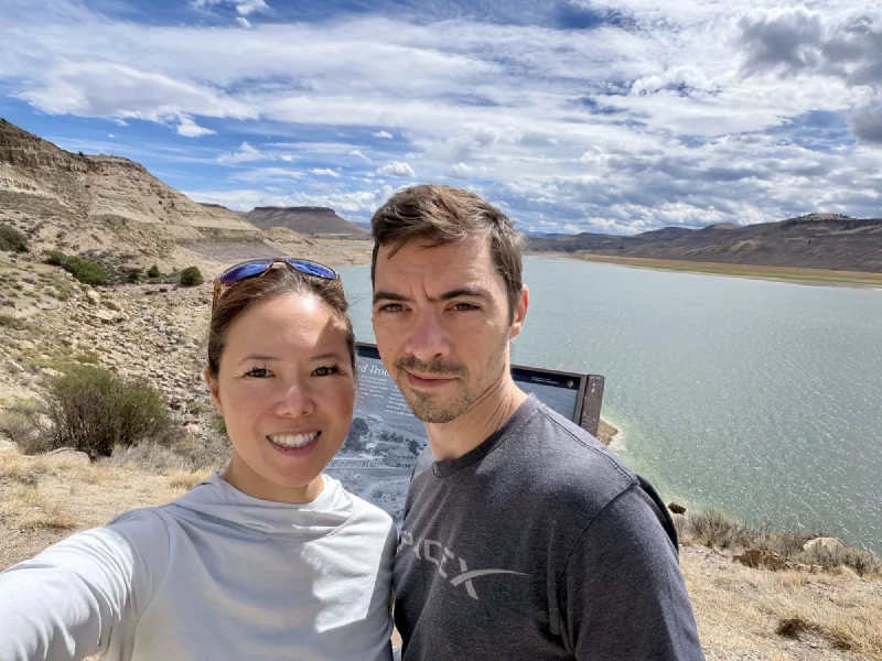 Pokin and Nicholas in a selfie at a reservoir overlook with an interpretive sign behind them