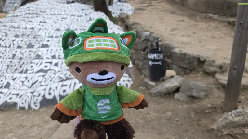Sumi at a mani stone with NAMCHE arrow on a nearby bin