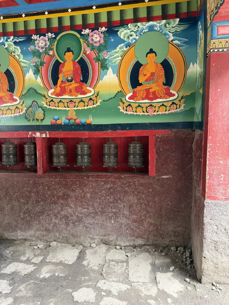 Colorful mani wall mural with three Buddhas and bronze prayer wheels