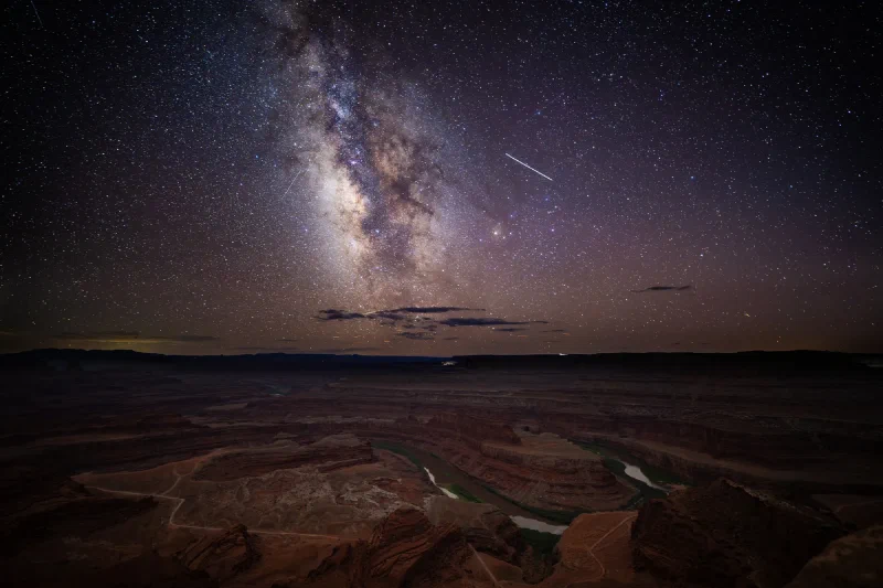 The Milky Way core rising over the Colorado River gooseneck at Dead Horse Point, with a bright streak across the sky