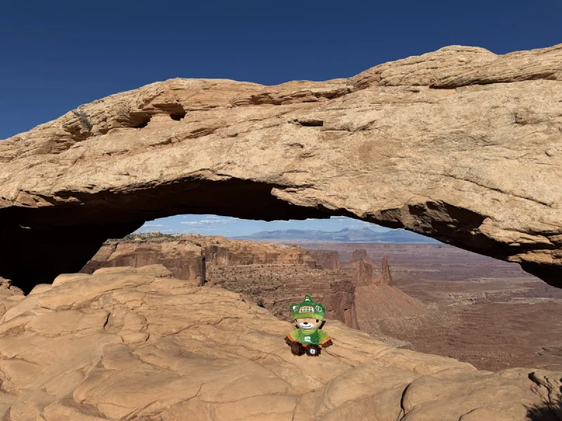 Sumi sitting on the slickrock under Mesa Arch with canyon country visible through the opening