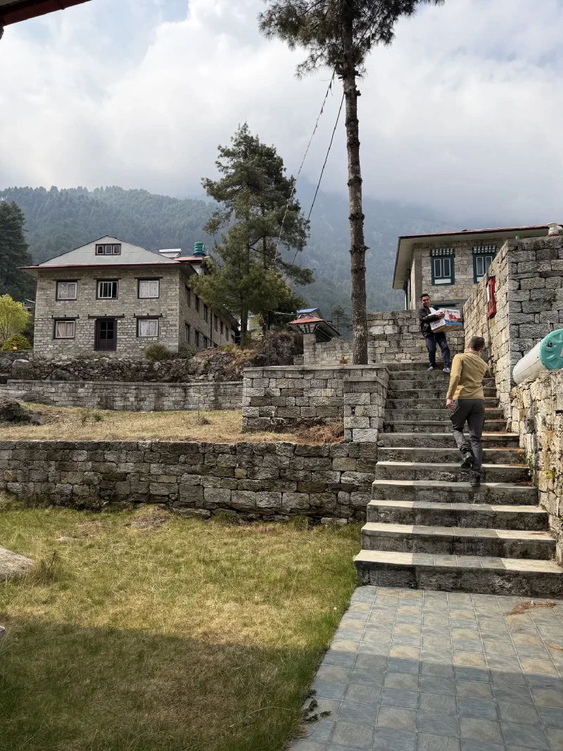 Nicholas walking up stone stairs while a local man carries a box of apples down