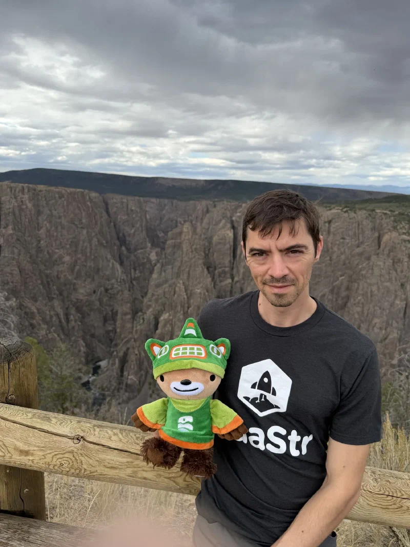 Nicholas holding Sumi at a log fence on the canyon rim, sheer grey walls dropping away behind and a river visible far below