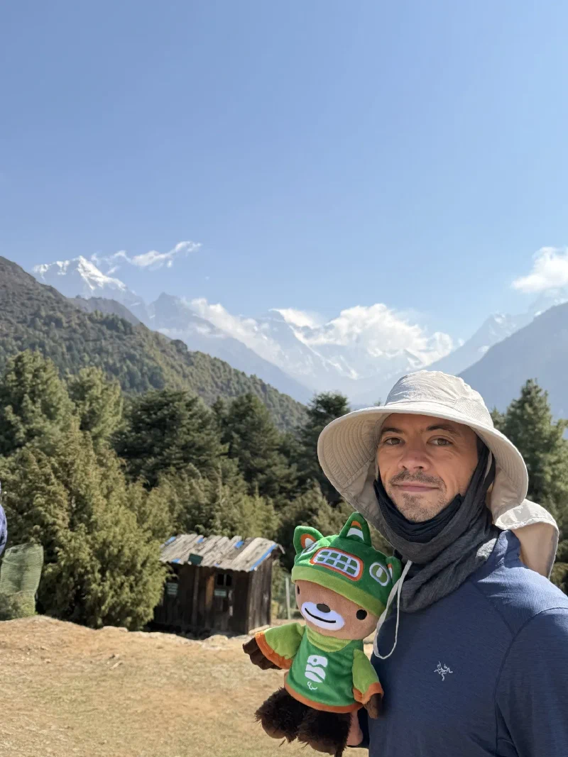 Nicholas holding Sumi Bear with snow-capped Himalayan peaks in background