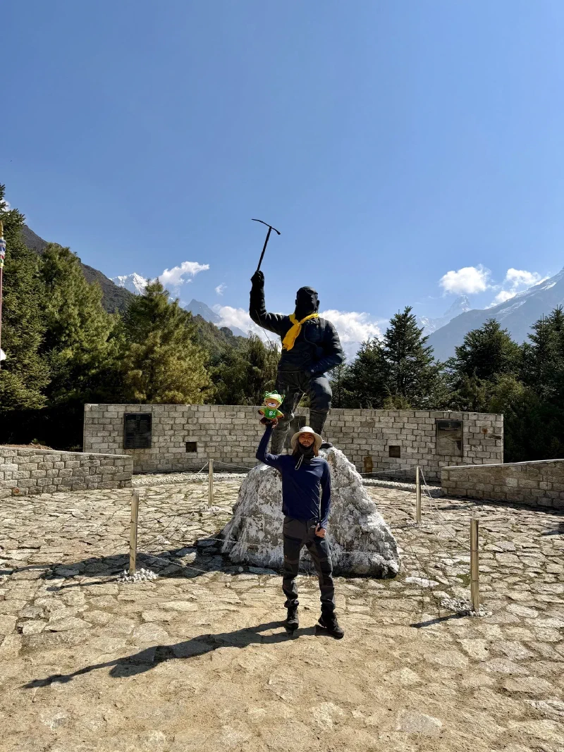 Nicholas holding Sumi Bear up at the Tenzing Norgay statue with peaks behind