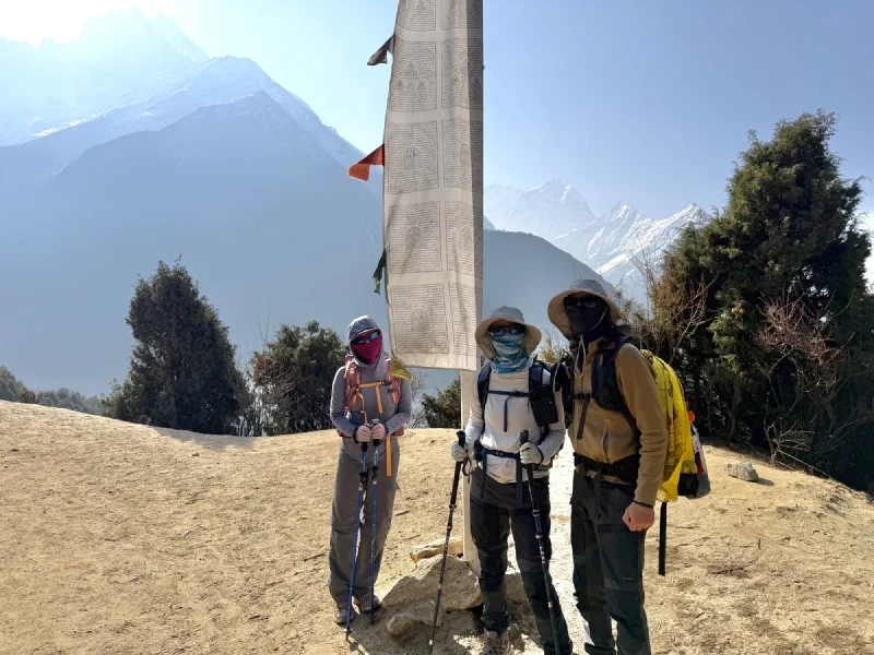 Three trekkers posing by a prayer flag