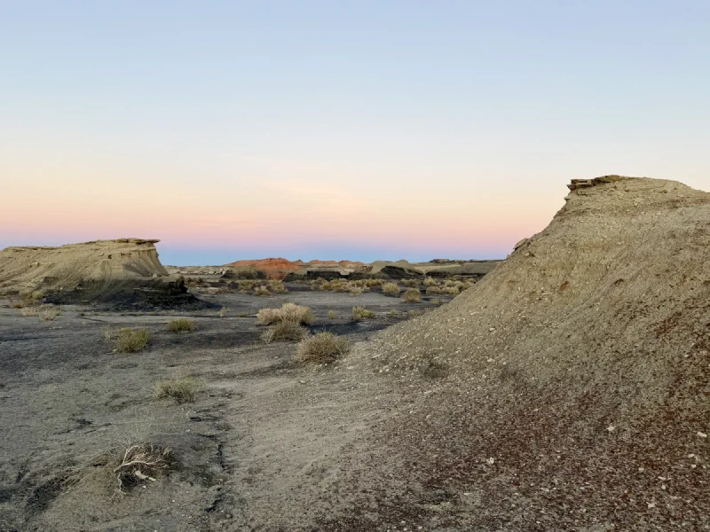 Eroded pale clay mounds capped with harder rock, with a red hill on the horizon under a pink and blue dusk sky