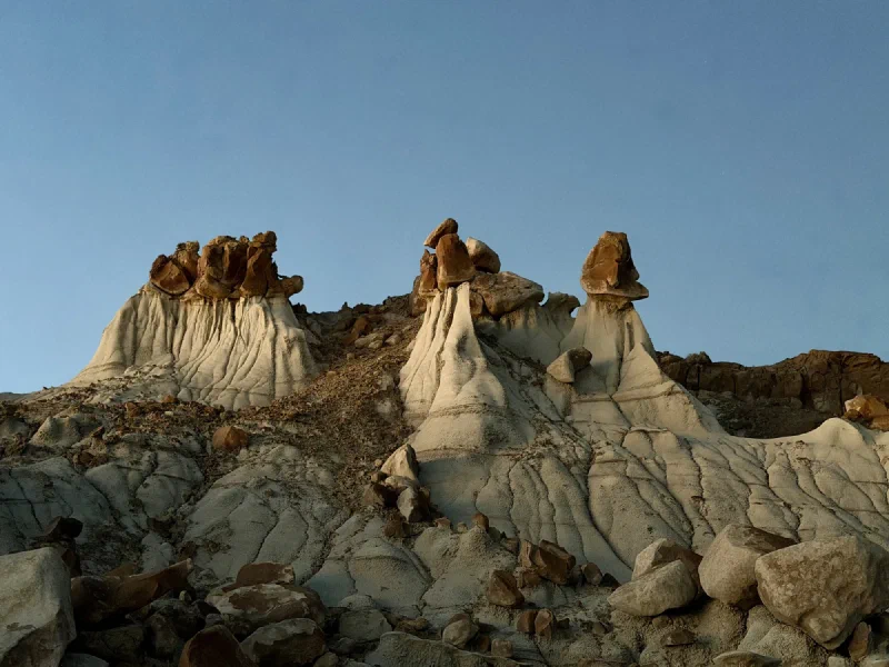 A row of hoodoos catching the last orange light, with brown boulder caps balanced on pale fluted clay spires