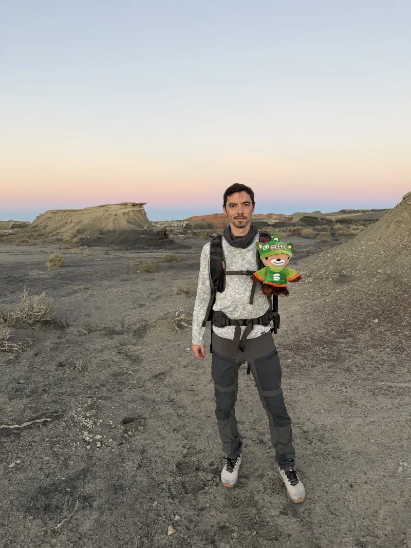 Nicholas standing in the badlands at dusk with a backpack on and Sumi strapped to the chest strap facing forward