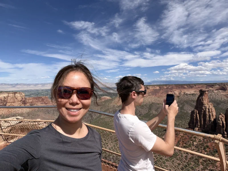 Pokin smiling in a selfie at the overlook railing while Nicholas photographs Independence Monument behind her