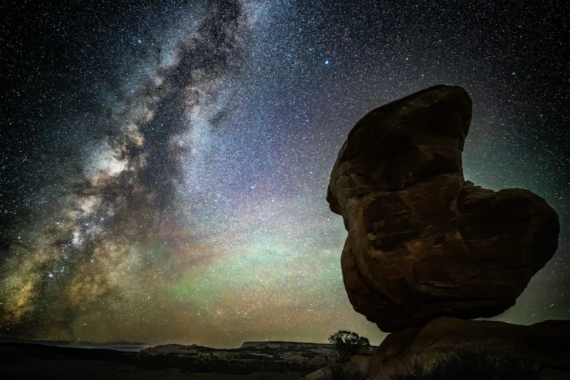 The Milky Way core arching over Miracle Rock in a dense field of stars with bands of green and pink airglow low in the sky
