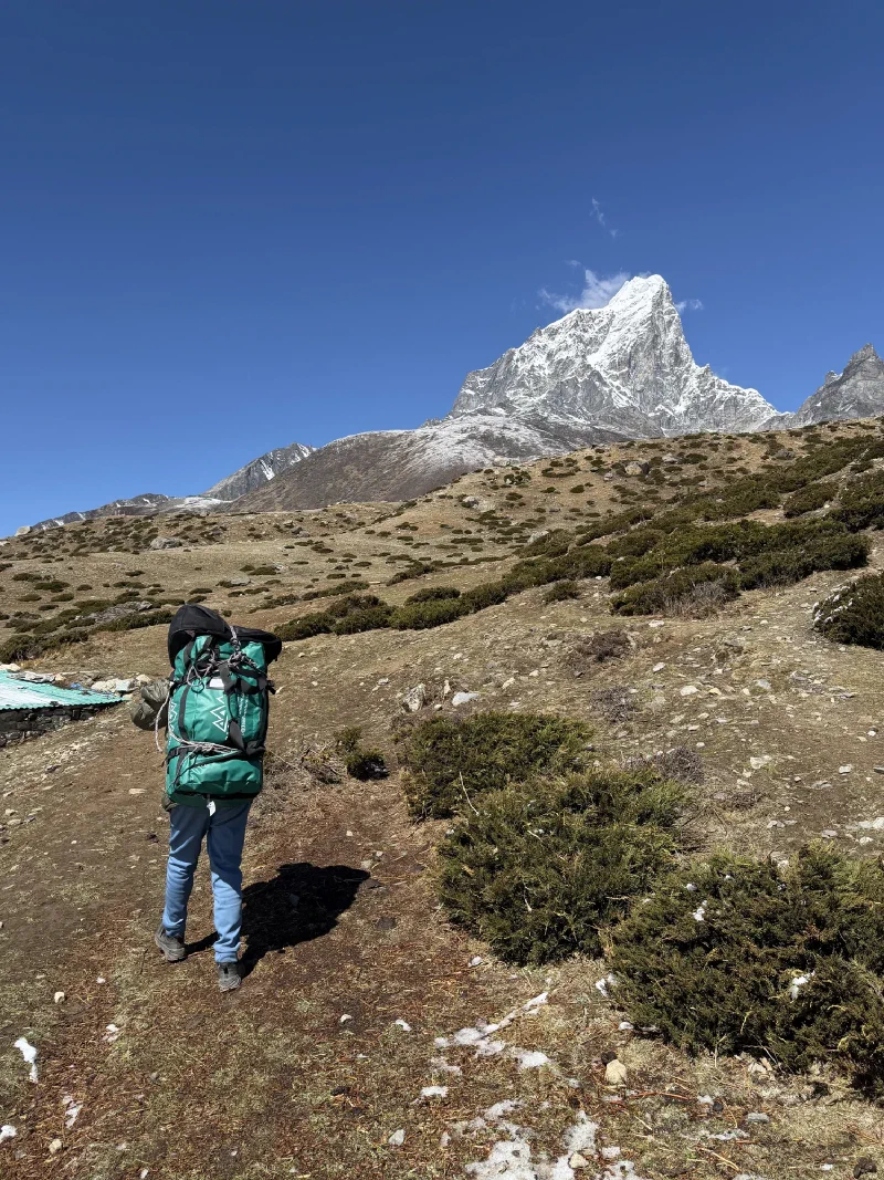 Nilman walking ahead on the trail with a large backpack, Ama Dablam behind