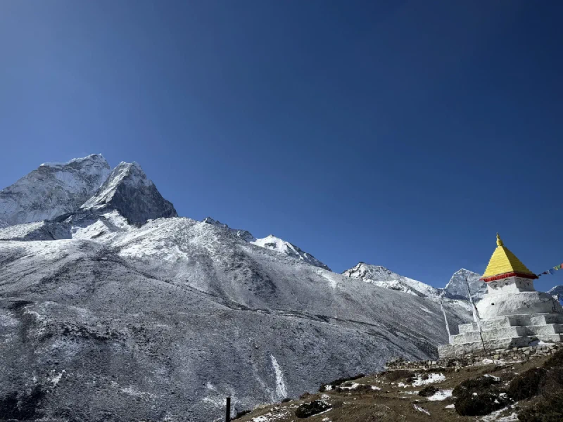 White Buddhist stupa with painted wisdom eyes against mountain backdrop