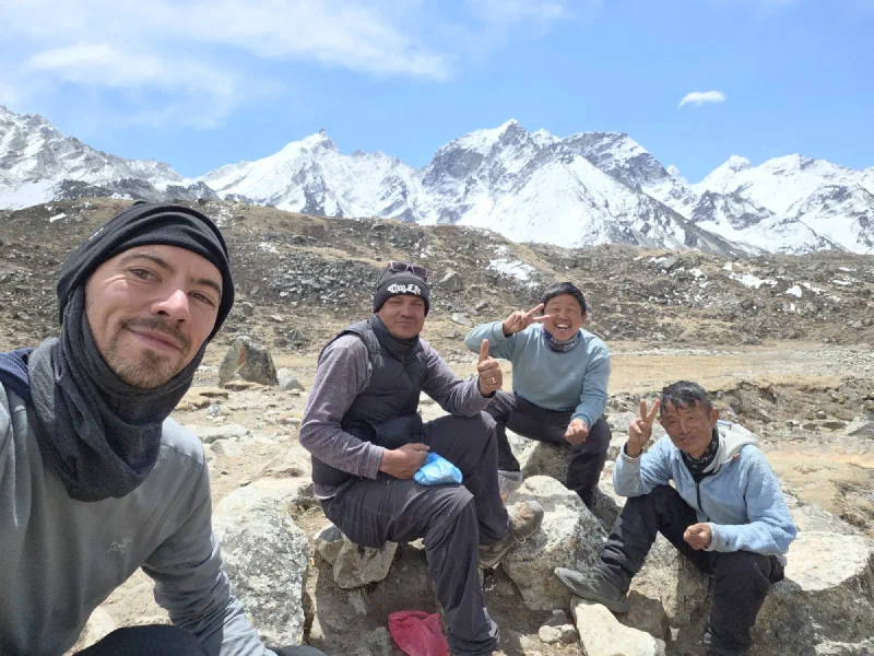Nicholas taking a selfie with three porters at a rest stop with snowy peaks behind
