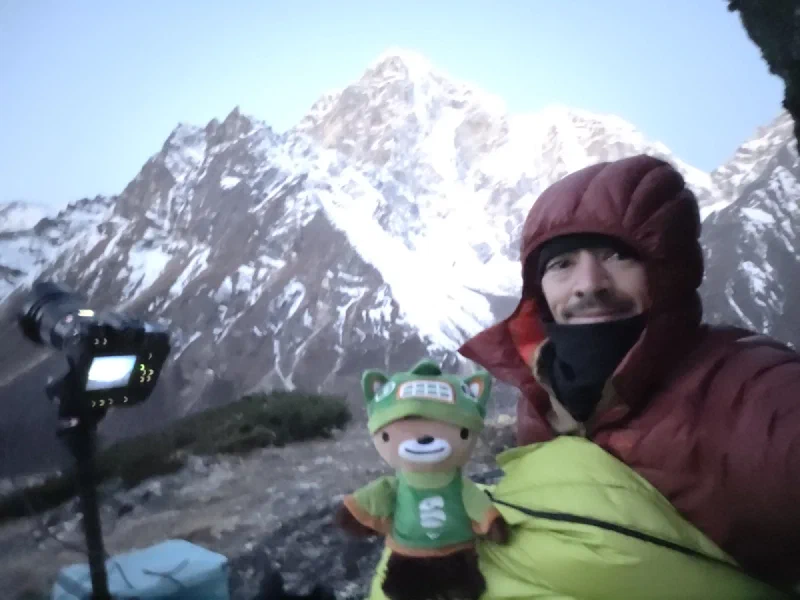 Nicholas bundled up at dawn holding Sumi with the camera on tripod and snowy peaks behind