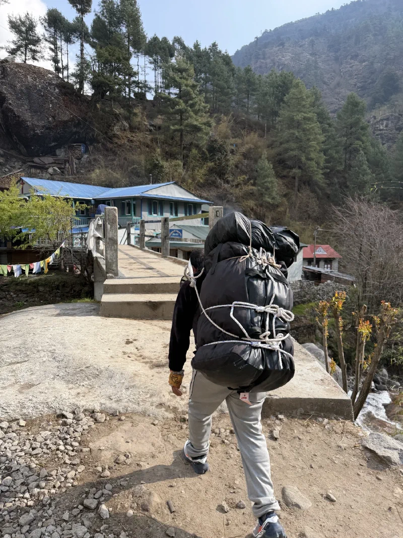 Porter carrying massive stack of duffel bags across a bridge