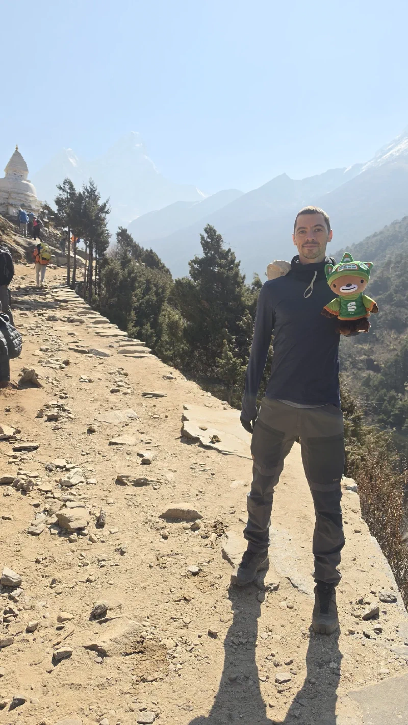 Nicholas holding Sumi on the trail with a white chorten behind