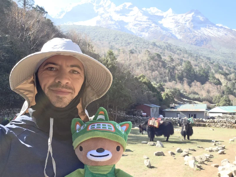 Nicholas holding Sumi with yaks and snow-capped mountains behind