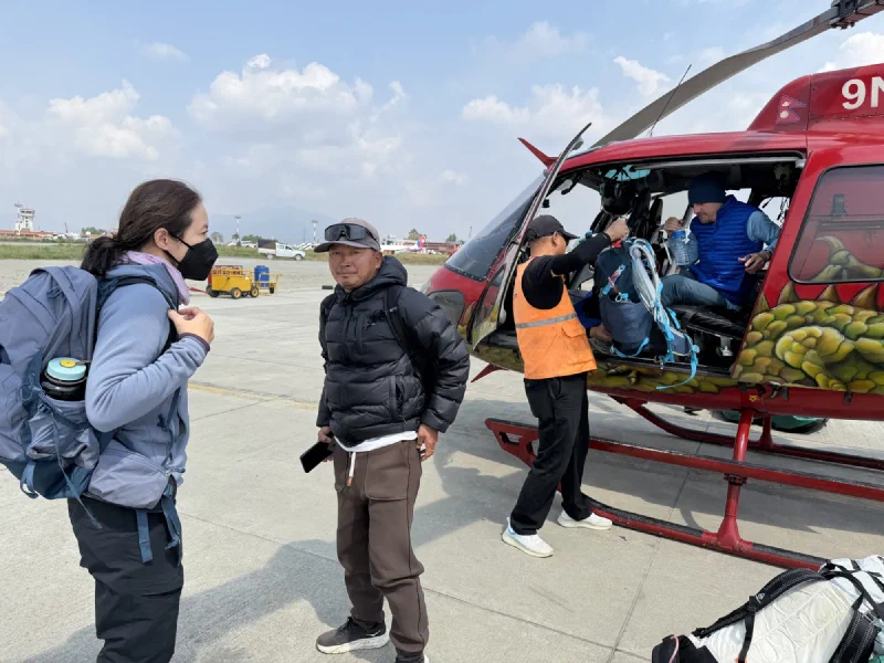 The group unloading gear from a red helicopter on the tarmac in Kathmandu