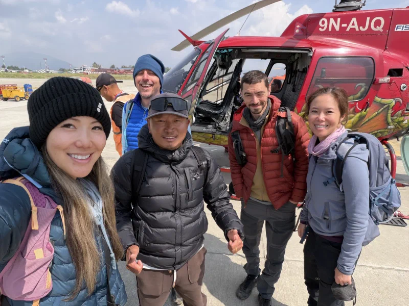The crew posing for a happy selfie in front of the red helicopter on the Kathmandu tarmac