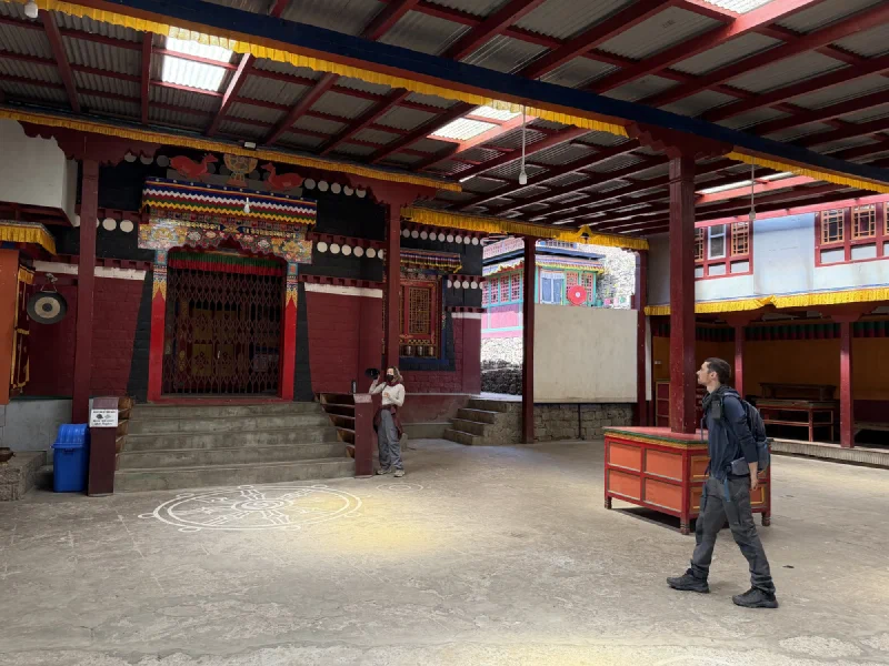Nicholas walking through a covered monastery courtyard with an intricate mandala design on the floor