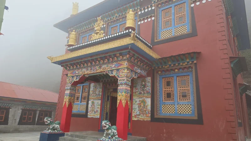 An ornate monastery entrance flanked by two carved stone lions, with a plainer building beside it