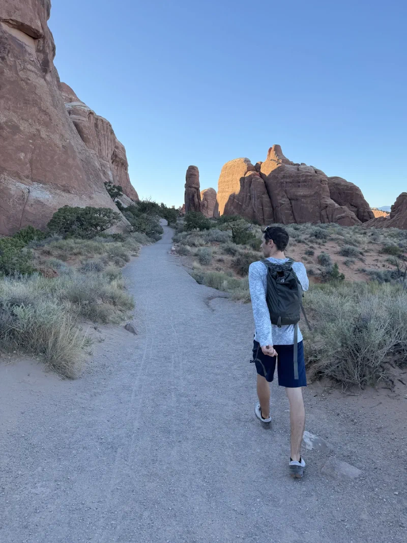 Nicholas walking away up a sandy trail between red fins with a pack on his back