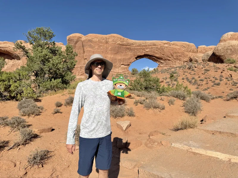 Nicholas in a wide-brimmed hat holding Sumi in front of the North Window arch
