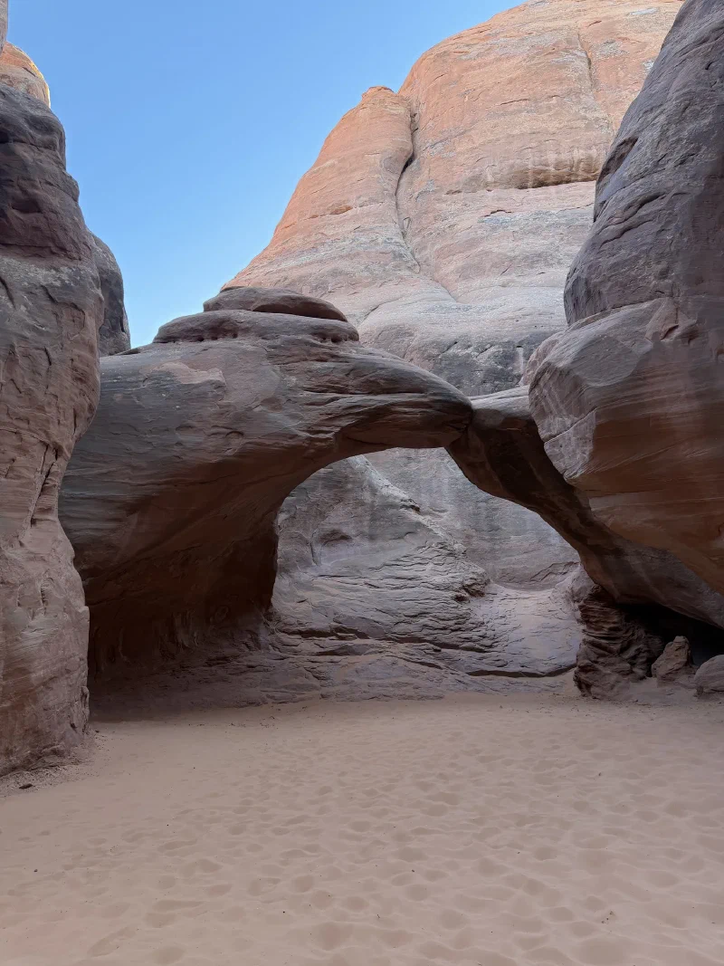 A small arch wedged between towering sandstone fins above a floor of deep pale sand