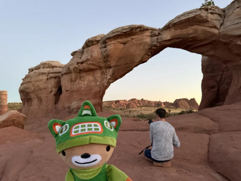 Sumi in close foreground with Nicholas kneeling under Broken Arch behind him at dusk