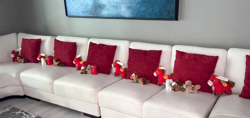 A stampede of brown and red stuffed horses arranged across the entire sofa with red pillows