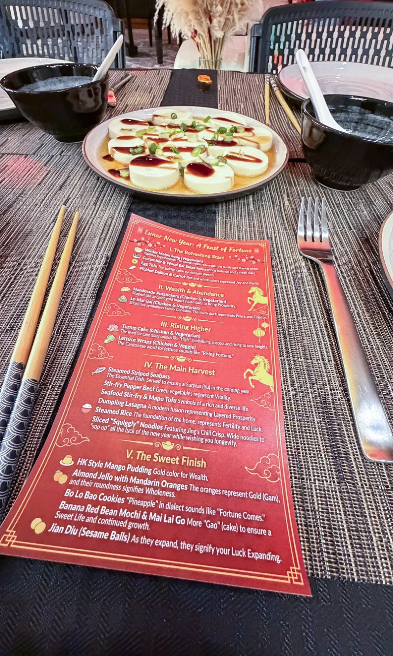 A red and gold Lunar New Year feast menu card with horse illustration at an elegant place setting